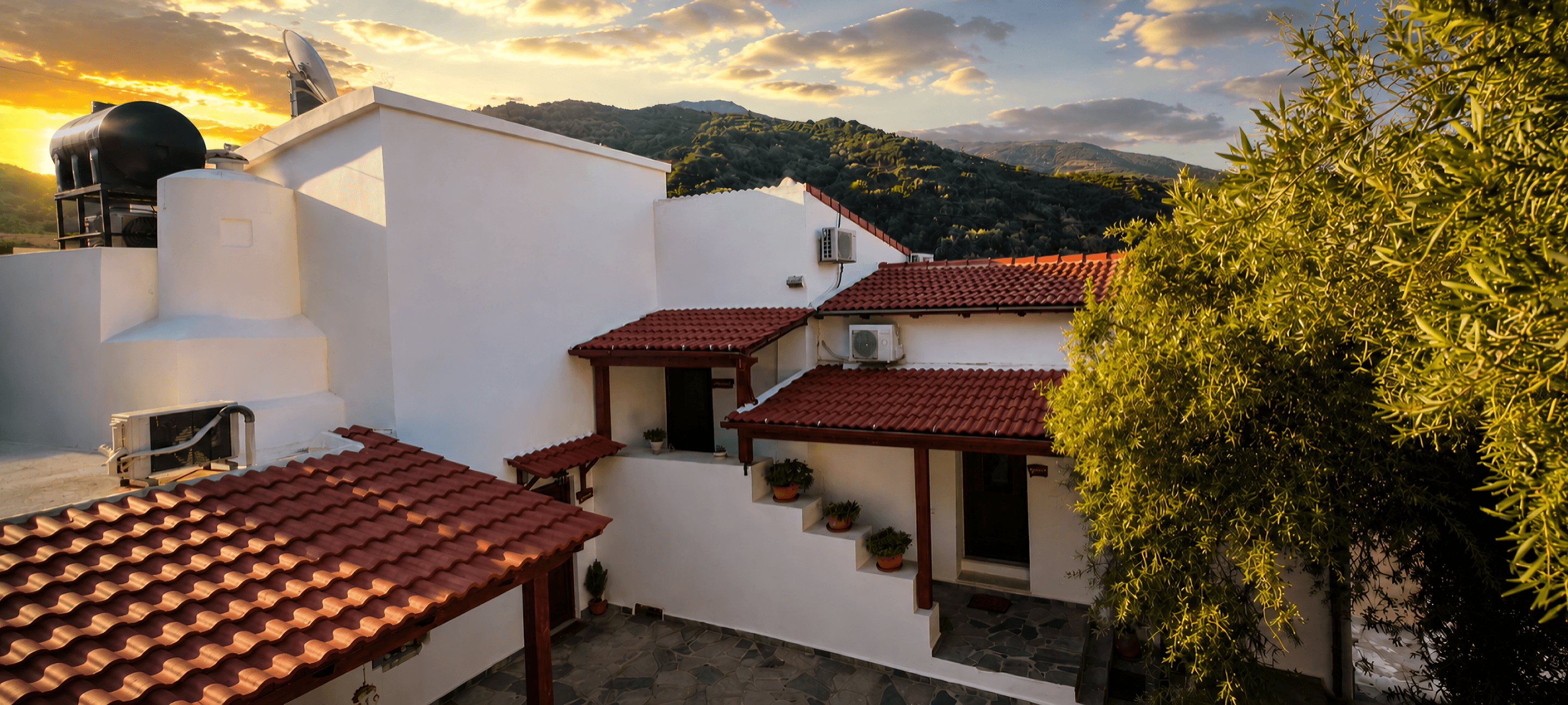 Aerial view of Plokamos House with traditional red-tiled roofs surrounded by olive trees and mountains